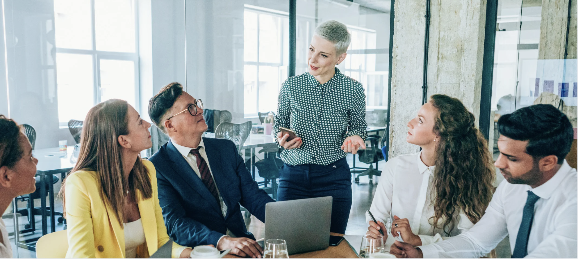 Group of employees in an office setting listening to a woman talk about retirement.