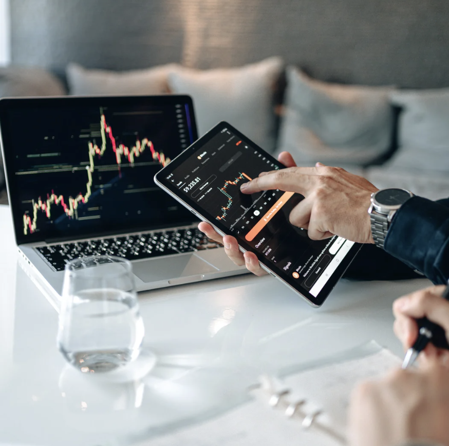 Person using a tablet and laptop displaying financial trading charts.